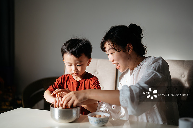 兴奋无忧的母亲和儿子在厨房里将鸡蛋打入搅拌碗中图片素材