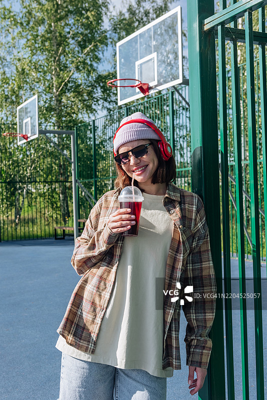 夏天在篮球场上，漂亮年轻女性喝果汁的肖像图片素材