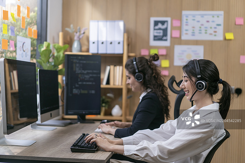 办公室内的呼叫中心操作员。女性呼叫中心代理与同事们在现代办公室工作。图片素材