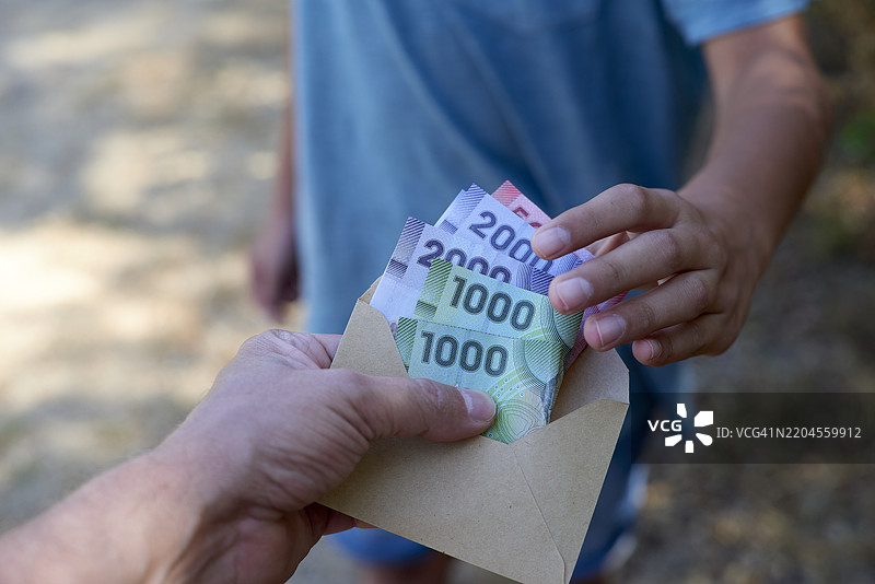 成年人将智利比索纸币放入信封中递给孩子图片素材