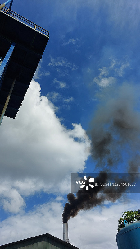 工业排放：黑烟在明亮的蓝天中翻滚图片素材