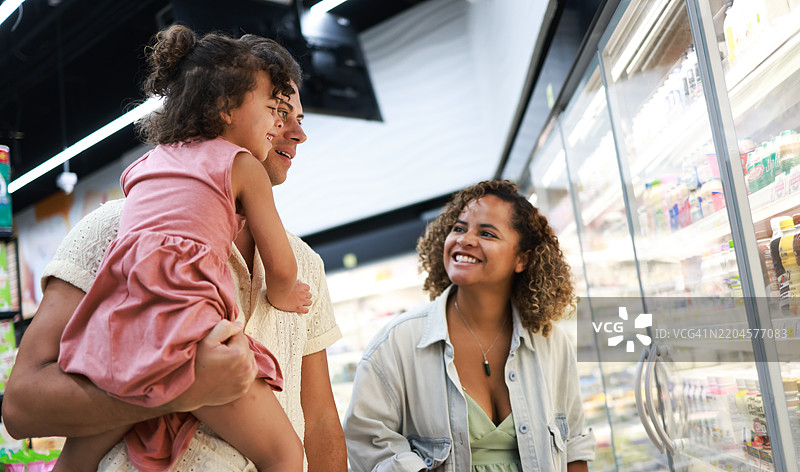 家庭在超市购物。快乐的父母和女儿在超市挑选商品。杂货店和购物概念。图片素材