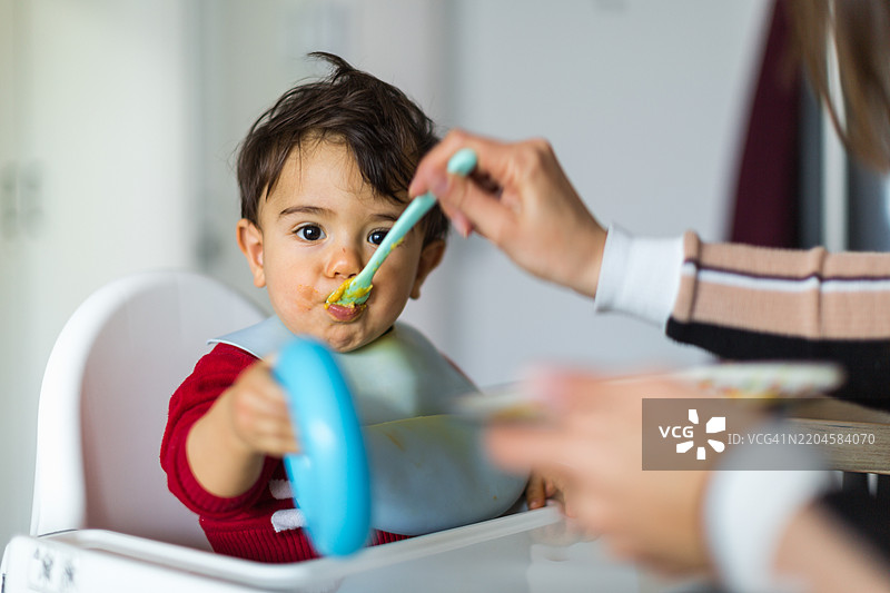 可爱宝宝在高脚椅上用勺子喂食图片素材