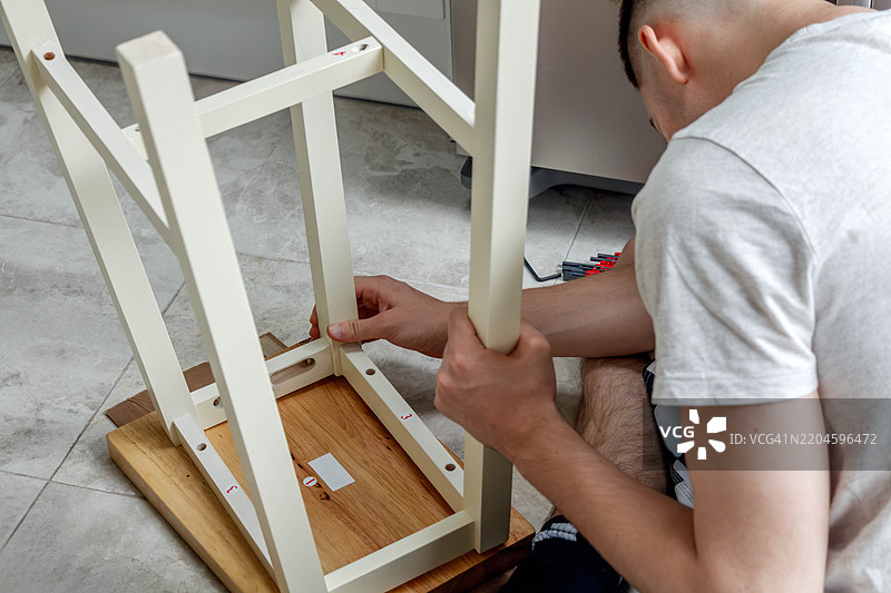 一名年轻男子正在折叠一把新的厨房吧椅图片素材