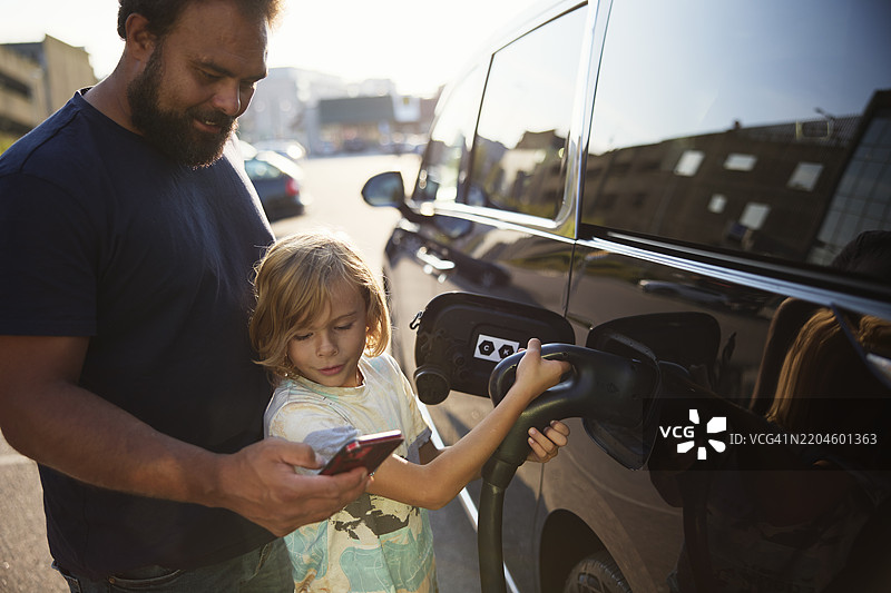 父亲在街上向正在充电的电动车的儿子展示智能手机。图片素材