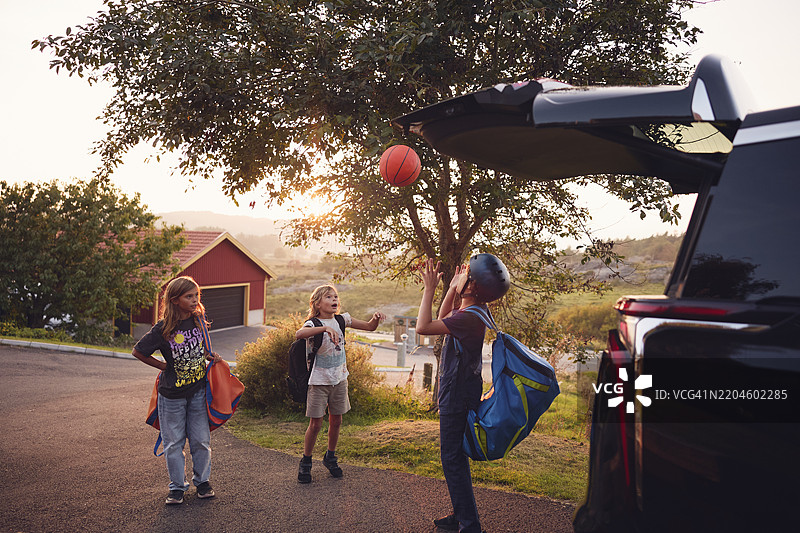 男孩戴着头盔，站在人行道上与兄弟姐妹一起向空中投掷球。图片素材