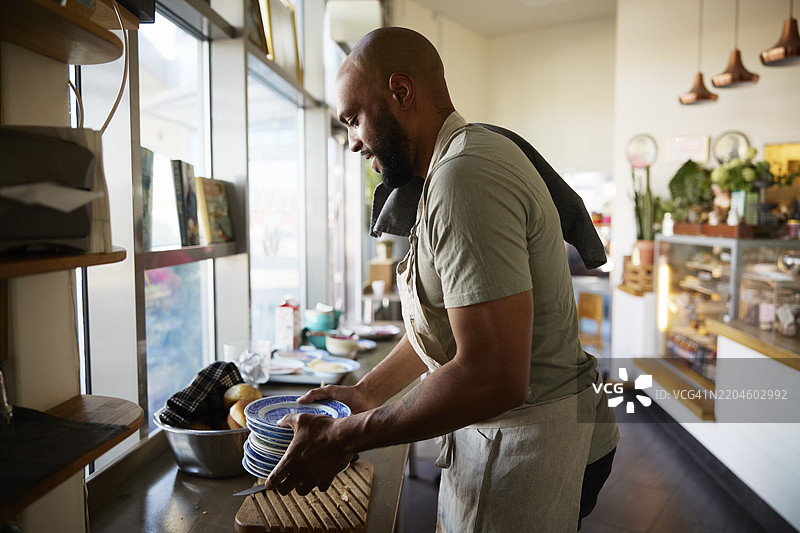 男性店主侧身拿着一叠盘子在咖啡馆工作图片素材
