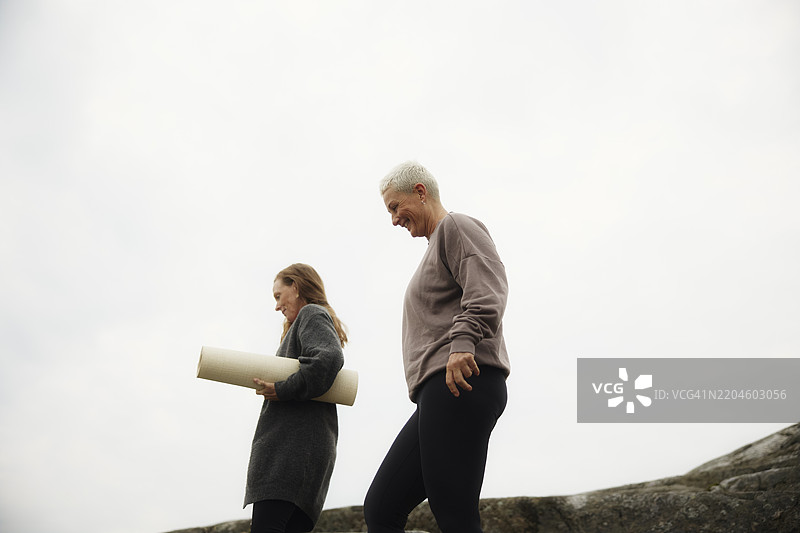 低角度视角的女性与朋友一起走，朋友手持瑜伽垫，背景是天空。图片素材