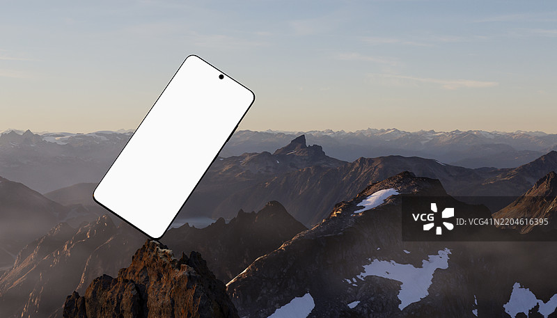 在日落时分，空白屏幕的智能手机平衡在山顶上图片素材