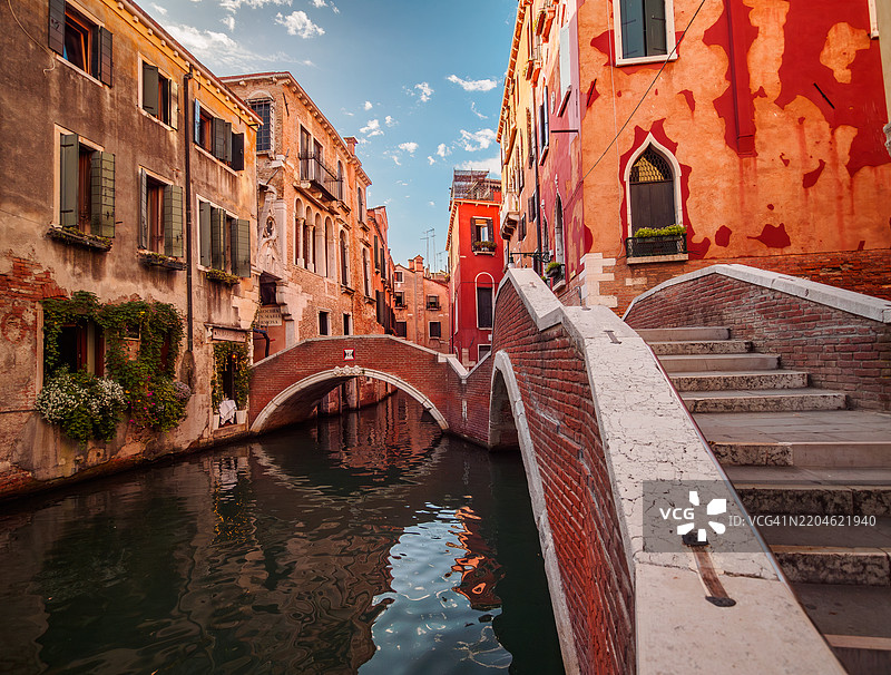 威尼斯卡斯特洛区一座空旷的双拱桥的广角视图，白天，五彩斑斓的红色住宅建筑在宁静的水面上倒影，联合国教科文组织世界遗产 - 威尼斯 - 威尼托 - 意大利。图片素材