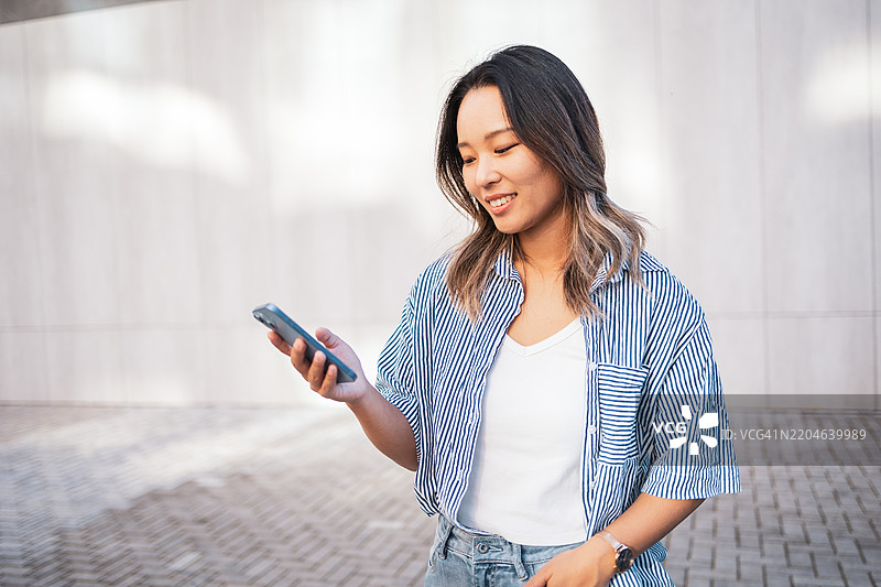 阳光明媚的户外，微笑的女性正在使用智能手机图片素材