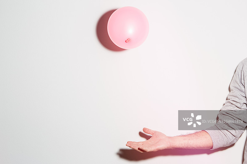 在白色墙壁前，伸出的手与弹跳的粉色气球图片素材