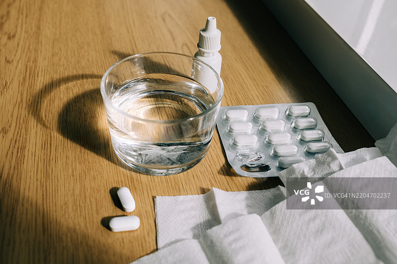 药丸、鼻喷雾、纸巾和一杯阳光照射下的水图片素材