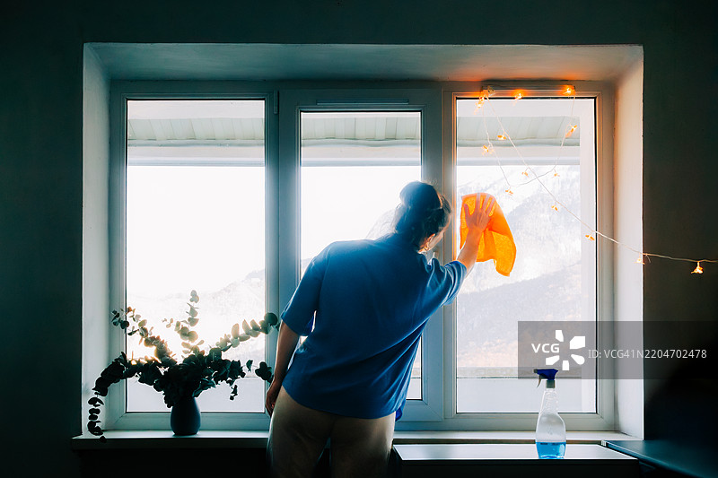 女人在明亮的公寓里用布和喷雾瓶清洁窗户图片素材
