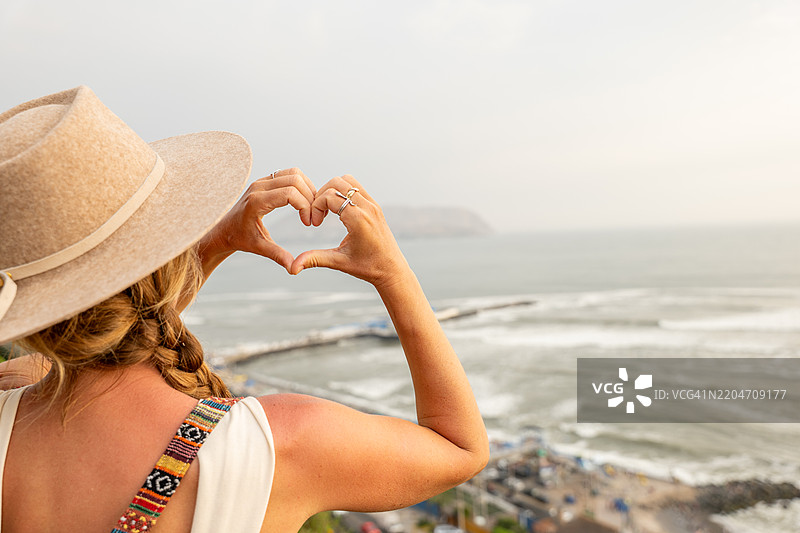女人用手做心形，俯瞰海洋景色图片素材