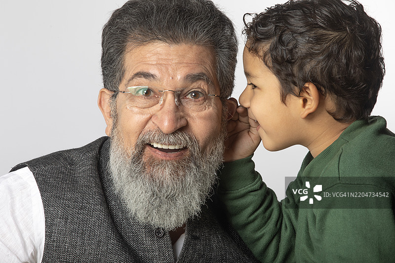 男孩在白色背景下向老年人耳边低语秘密图片素材