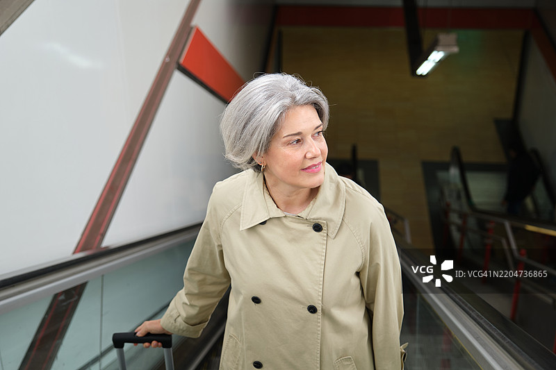 一位老年女性在地铁站的自动扶梯上推着她的手推车。图片素材