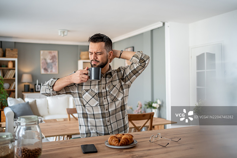 困倦的男人在早餐台喝咖啡并伸展身体图片素材