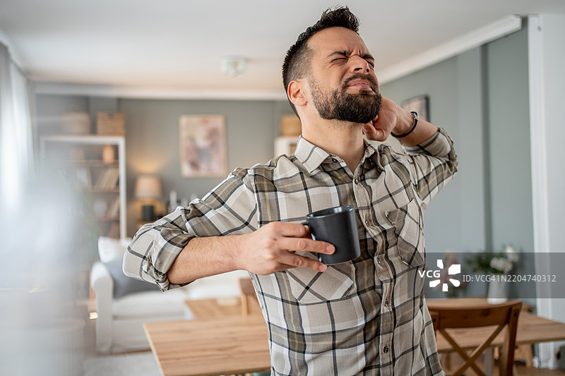 在家喝咖啡并感到颈部疼痛的男人图片素材