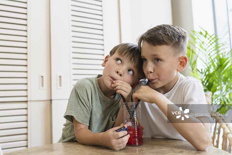 兄弟们在家里用吸管共享一杯果汁图片素材