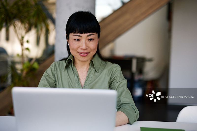 现代办公室中工作的日本女商人使用笔记本电脑图片素材