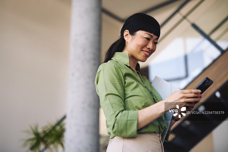 日本女商人在办公大楼内使用智能手机并手持文件图片素材
