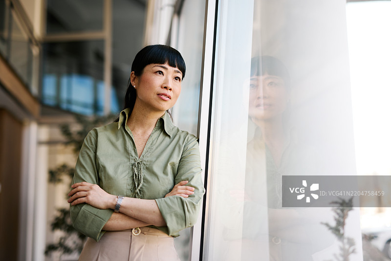 沉思的日本女商人在现代办公室靠窗而立图片素材