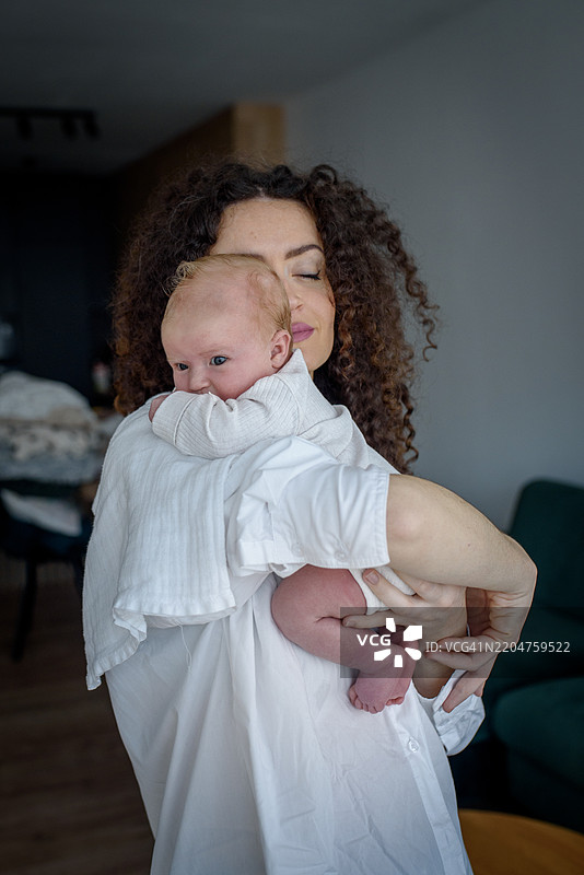 卷发母亲将新生儿抱在肩上。图片素材