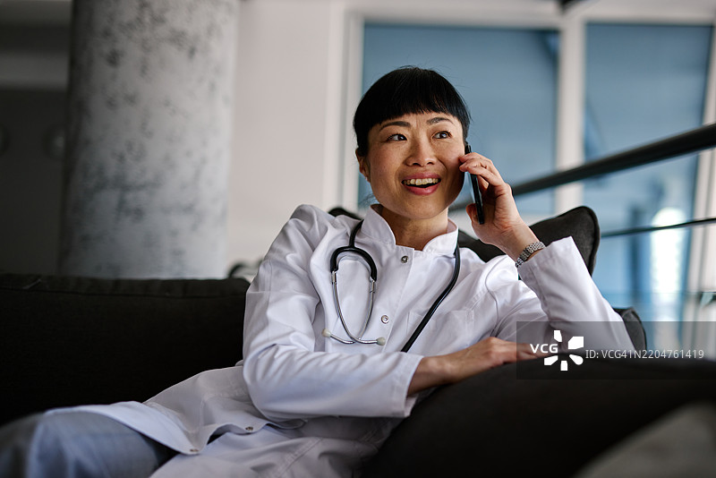 日本女性医生在沙发上放松，打电话。图片素材
