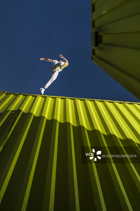 年轻男子在蓝天下跳过绿色货运集装箱图片素材