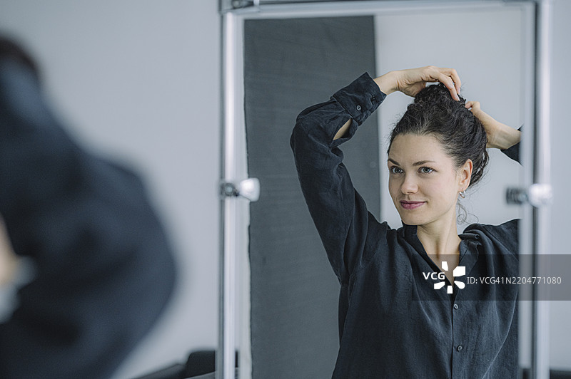 微笑的女性在家中扎头发并照镜子图片素材