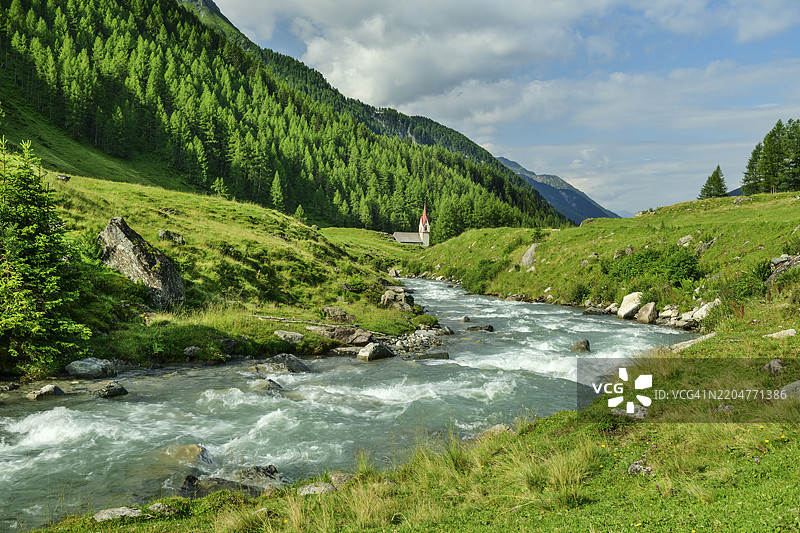 意大利，里泽尔费尔纳山脉的阿赫河，附近有一座小教堂，天空多云。图片素材