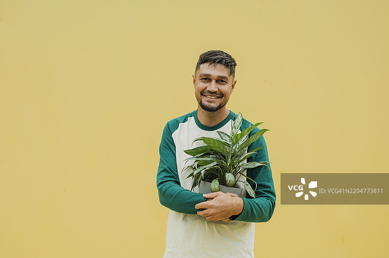 成熟男性在橙色背景下手持盆栽植物图片素材