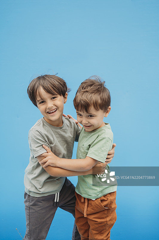 微笑的小兄弟们在蓝色背景下相拥图片素材
