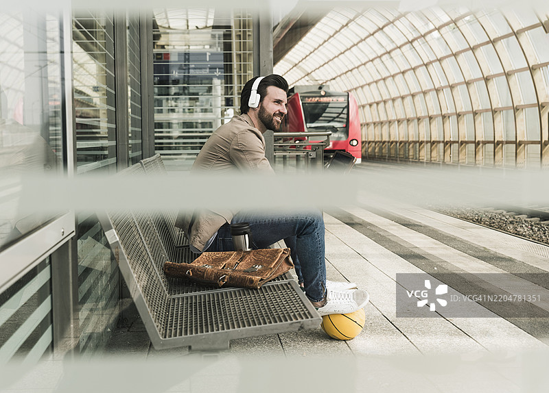 戴着耳机的男子在火车站坐着，手里拿着篮球图片素材