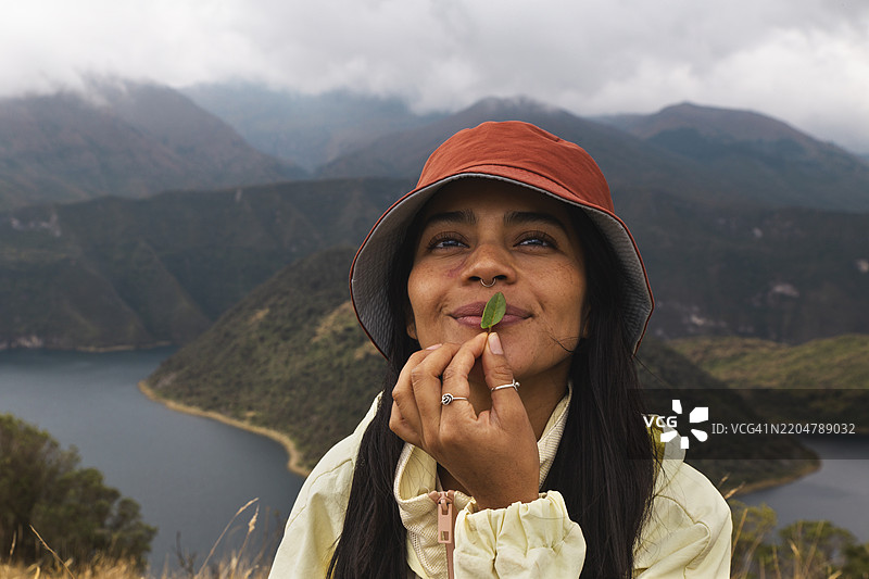 微笑的女性戴着渔夫帽，嘴唇上夹着一片叶子图片素材