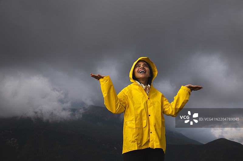 无忧无虑的女性穿着雨衣，在阴 cloudy 的天空下尽情享受图片素材