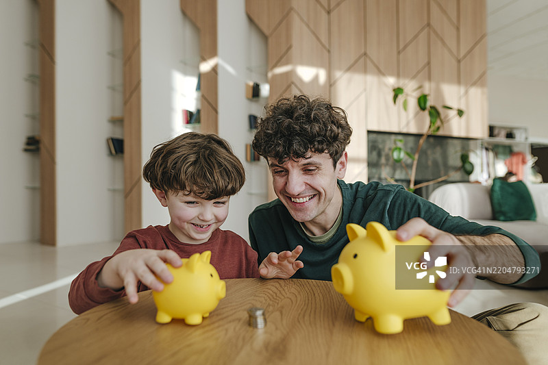 快乐的父亲和儿子在家里玩储蓄罐图片素材