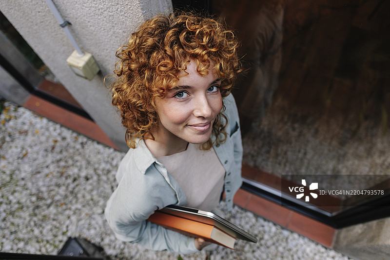 一位卷发女性手持笔记本电脑站在小巷中图片素材
