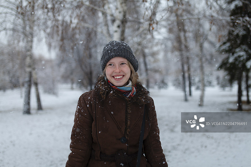 微笑的女性穿着温暖的衣服，站在冬季森林中图片素材