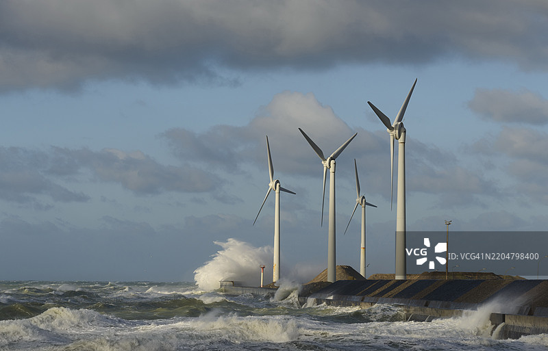 在阴云密布的天空下，海浪拍打着风力涡轮机图片素材