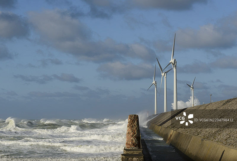 暴风雨中的海浪拍打着靠近风力涡轮机的挡墙，天空阴云密布图片素材