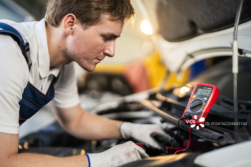汽车技师在车间使用电压表检查打开引擎盖的车辆图片素材