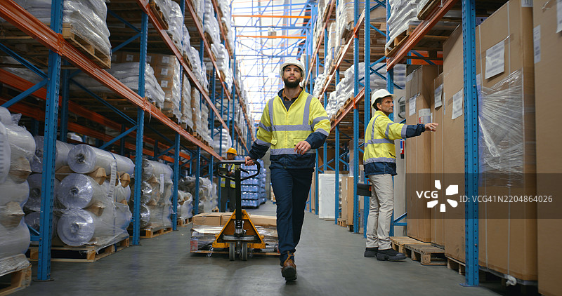 男性在仓库中走动，推着手推车进行配送服务、存储管理和物流。男性正在检查和移动供应链的包裹，进行库存交付和行业装载。图片素材