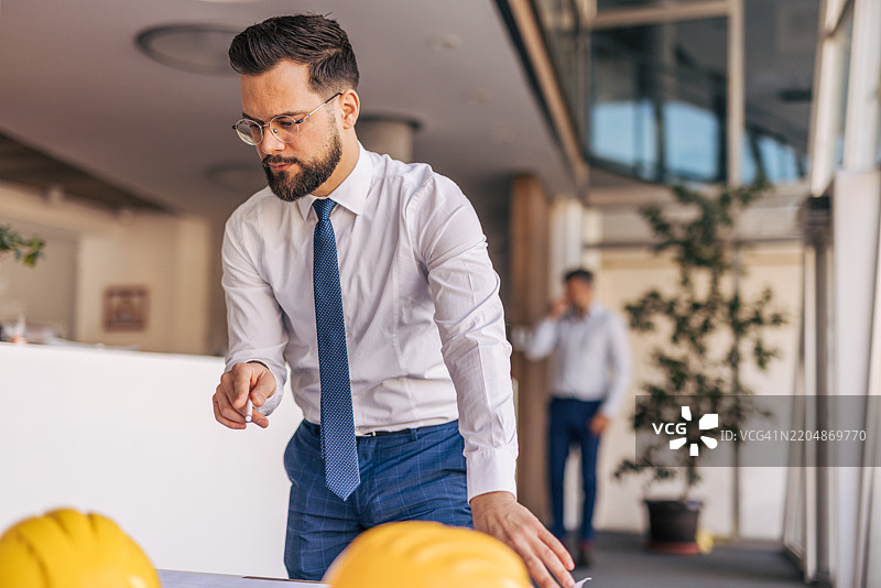 建筑师在桌子上查看蓝图，旁边有安全头盔图片素材