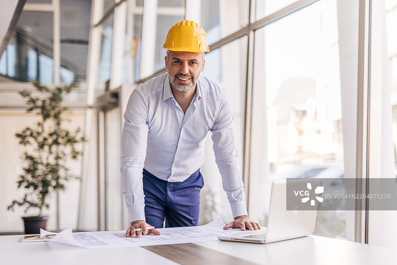 在办公室里，戴着安全帽的建筑师对着镜头微笑图片素材
