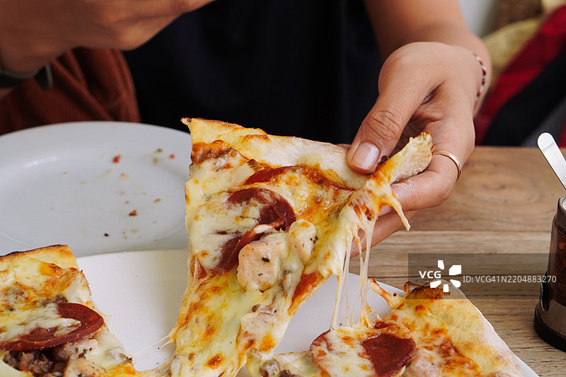 女人的手正在拿起一片新鲜出炉的肉食爱好者披萨图片素材