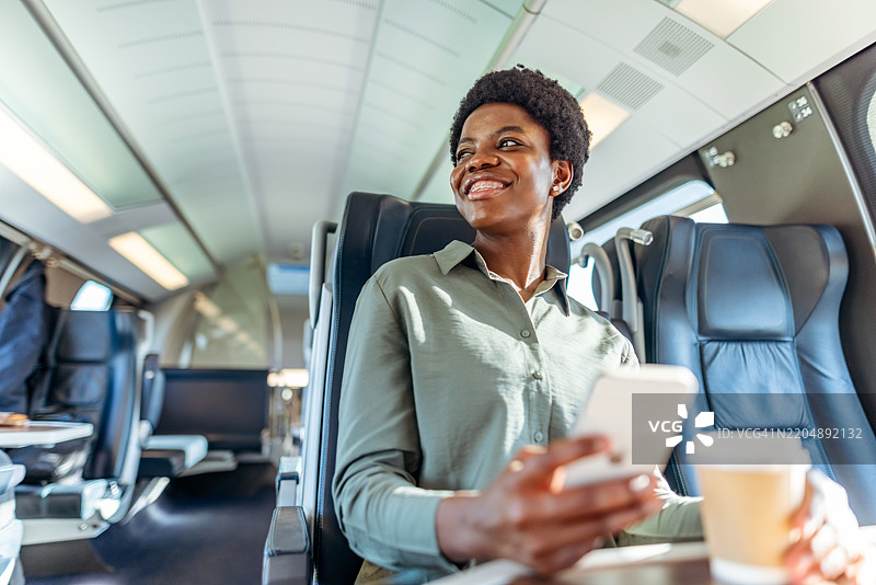 微笑的女性在火车上使用智能手机和喝咖啡图片素材