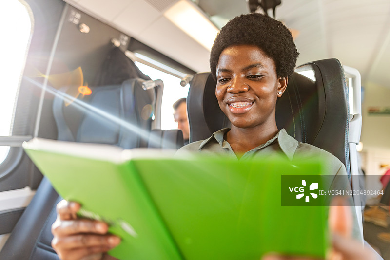 微笑的年轻女性在火车上阅读一本书图片素材