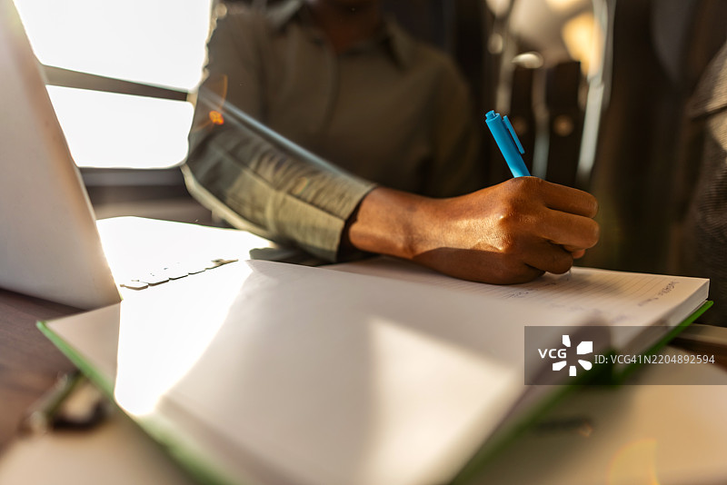 在阳光明媚的工作空间里，正在用笔记本电脑写笔记的人图片素材